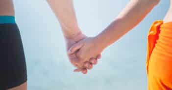 Midsection of Couple Holding Hands at Beach Against Sky