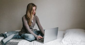 woman typing on MacBook Pro while sitting on bed in room