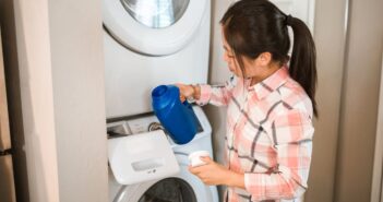 A Woman Wearing a Checkered Long Sleeves Holding a Blue Plastic Bottle Near a Washing Machine