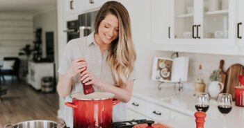 smiling woman standing and putting pepper on stock pot