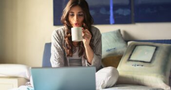 Woman in Grey Jacket Sits on Bed Uses Grey Laptop