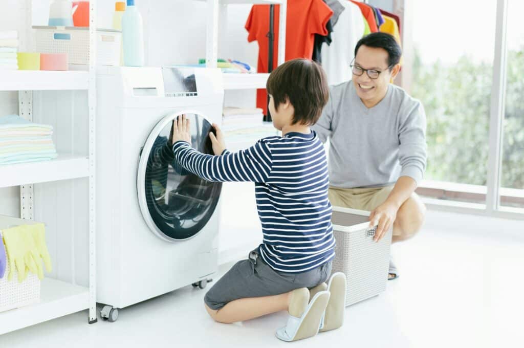 Happy smiling Asian family father and son in the laundry load a washing machine. Family activity.