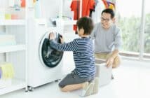 Happy smiling Asian family father and son in the laundry load a washing machine. Family activity.