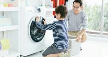 Happy smiling Asian family father and son in the laundry load a washing machine. Family activity.