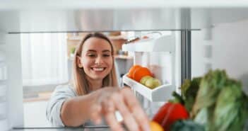 Happy woman taking vegetable from the fridge