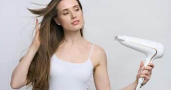 Isolated portrait on white backdrop of young woman blowing warm air fron hair dryer on long wet hair