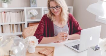 woman smiling holding glass mug sitting beside table with MacBook