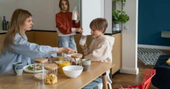 Loving teenage daughter holding bottle of milk from fridge for family breakfast with mom and brother