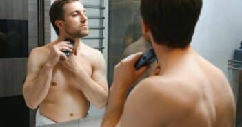 Reflection of young man in mirror shaving with electric shaver