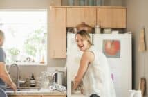 Smiling blond woman standing at a fridge in a kitchen.