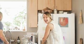 Smiling blond woman standing at a fridge in a kitchen.