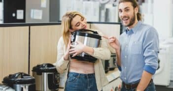 smiling consultant pointing with finger at woman with slow cooker in home appliance store