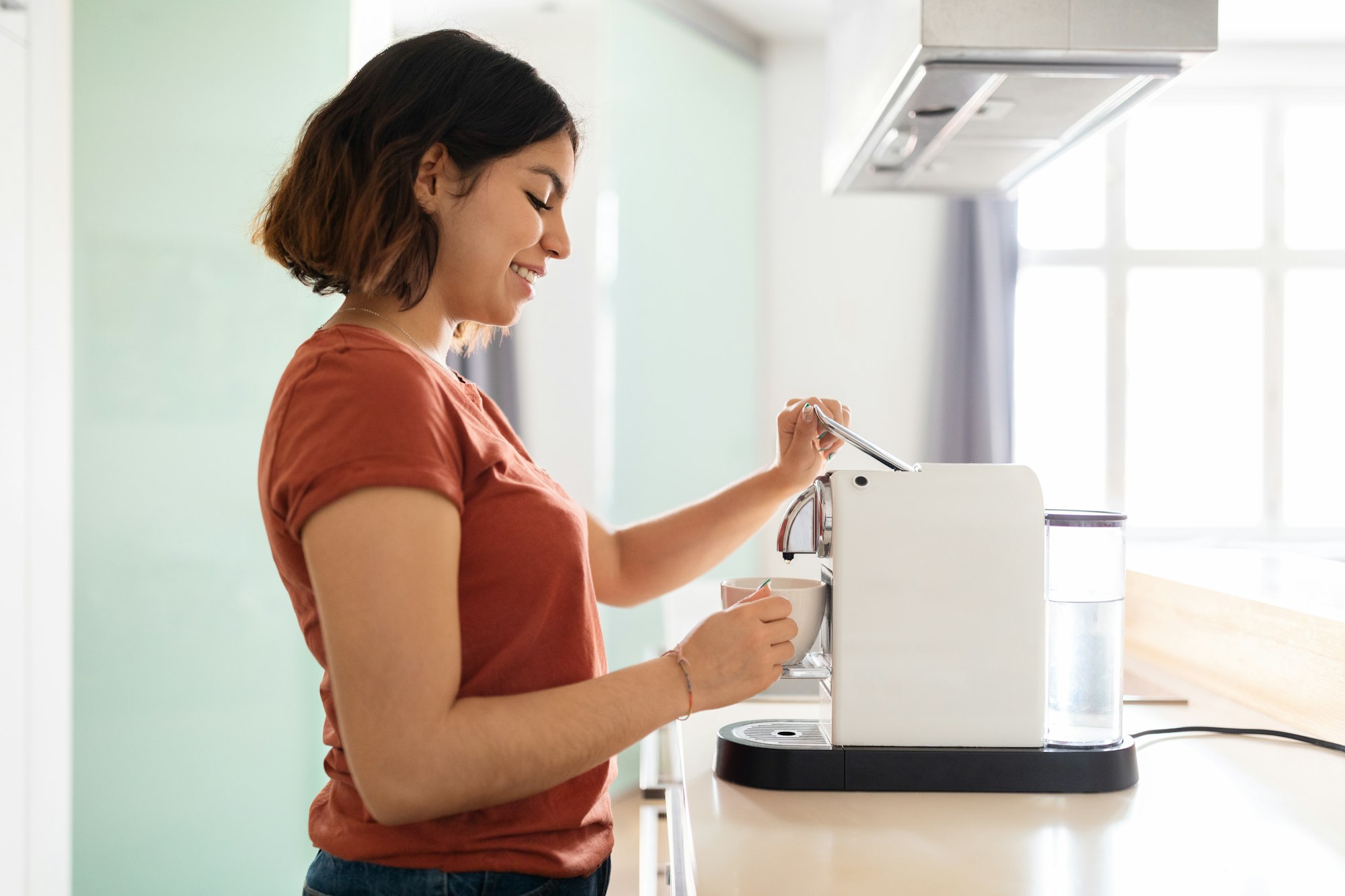 Young smiling arab woman preparing fresh coffee with modern machine in kitchen