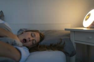 Young woman lying in bed at home at night yawning