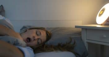 Young woman lying in bed at home at night yawning