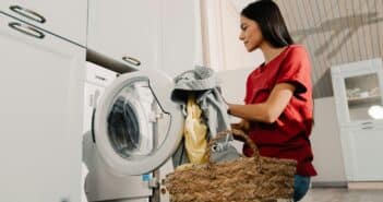 Young woman putting clothes at washing machine while doing laundry