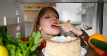 Cheerful woman tasting cake with finger in fridge