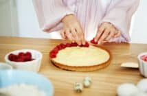 Chef Woman decorating cake with berries and cream cheese on kitchen table