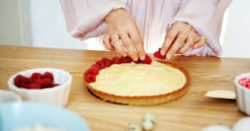 Chef Woman decorating cake with berries and cream cheese on kitchen table