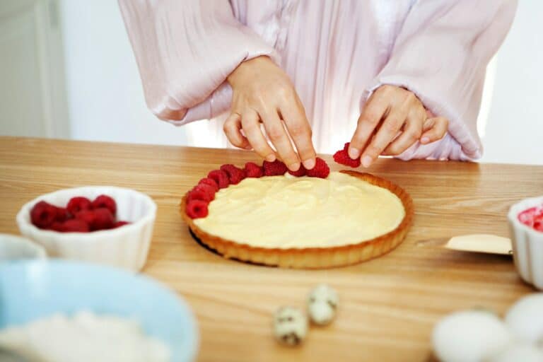 Chef Woman decorating cake with berries and cream cheese on kitchen table