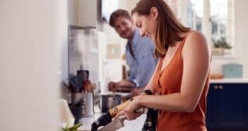 Couple With Woman With Prosthetic Arm In Kitchen Preparing Meal Together