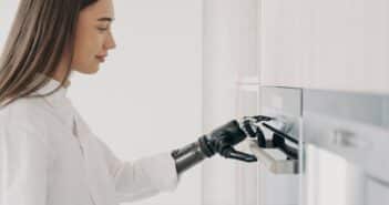 Happy disabled woman with robotic cyber hand switching oven on. Cooking at home using bionic limb.