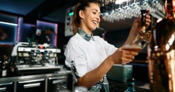 Happy female barista pouring beer from a beer tap while working in pub.