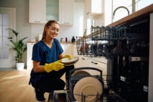 Happy woman putting dishes in the dishwasher.