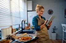 Happy woman reading a recipe on touchpad while preparing food in the kitchen.