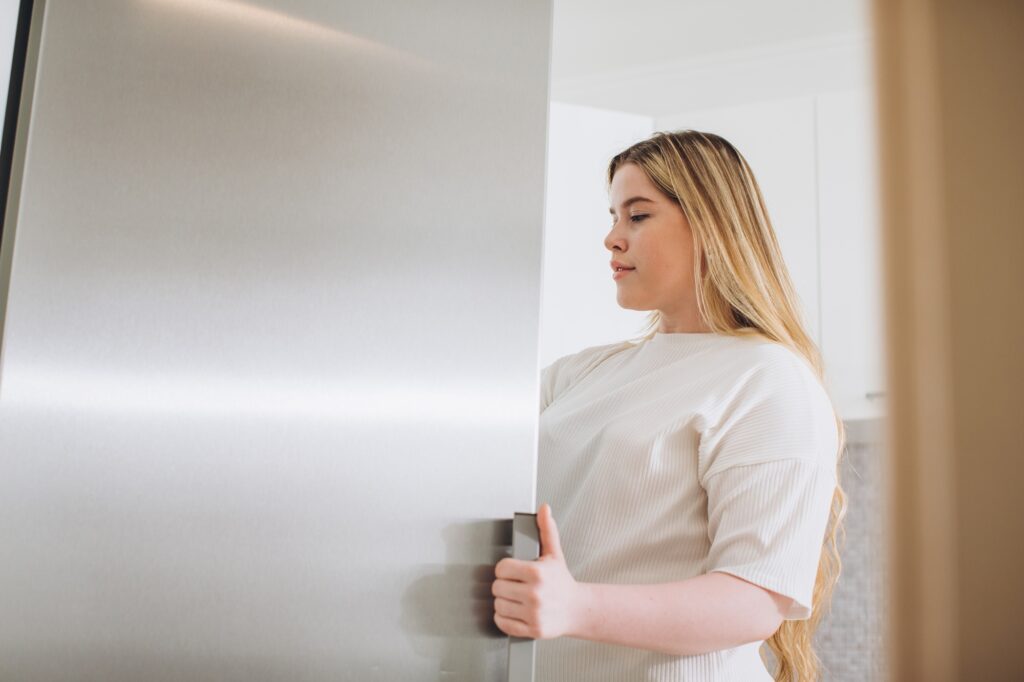 Happy young woman standing at the opened fridge