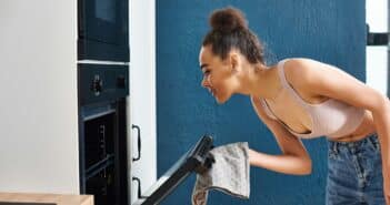 joyous beautiful african american woman in homewear using oven to bake while at home in kitchen