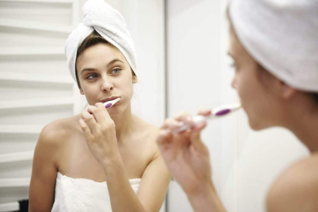 Mirror image of young woman in bathroom brushing her teeth