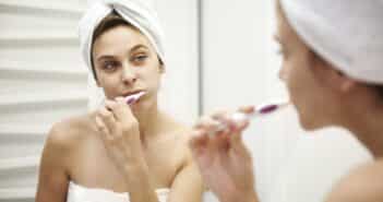 Mirror image of young woman in bathroom brushing her teeth