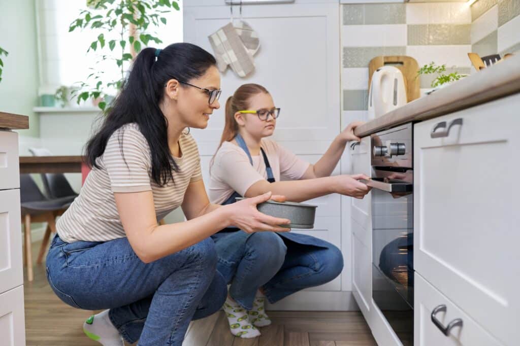 Mother and daughter preparing cake together, putting mold with dough in oven