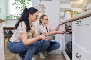 Mother and daughter preparing cake together, putting mold with dough in oven