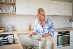 Senior woman loading or unloading dishwasher indoors at home