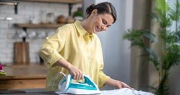 Smiling beautiful housewife ironing the wrinkled shirt