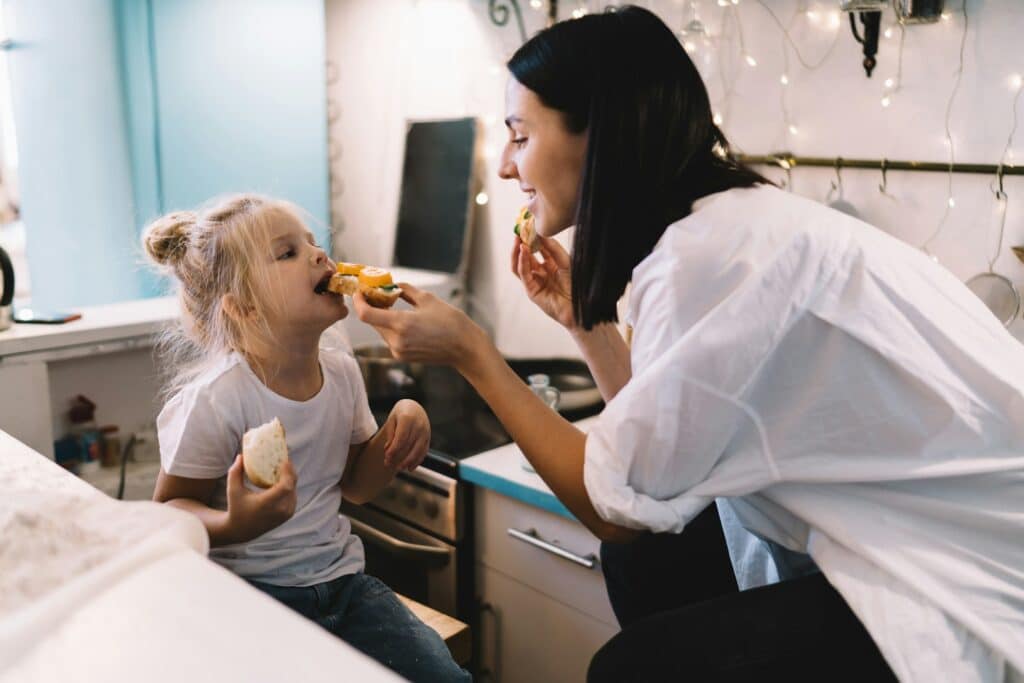 Woman and girl feeding each other in kitchen