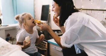 Woman and girl feeding each other in kitchen