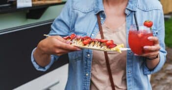 Woman enjoys delicious pancakes with strawberries and strawberry daiquiri at food festival.