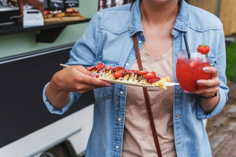 Woman enjoys delicious pancakes with strawberries and strawberry daiquiri at food festival.