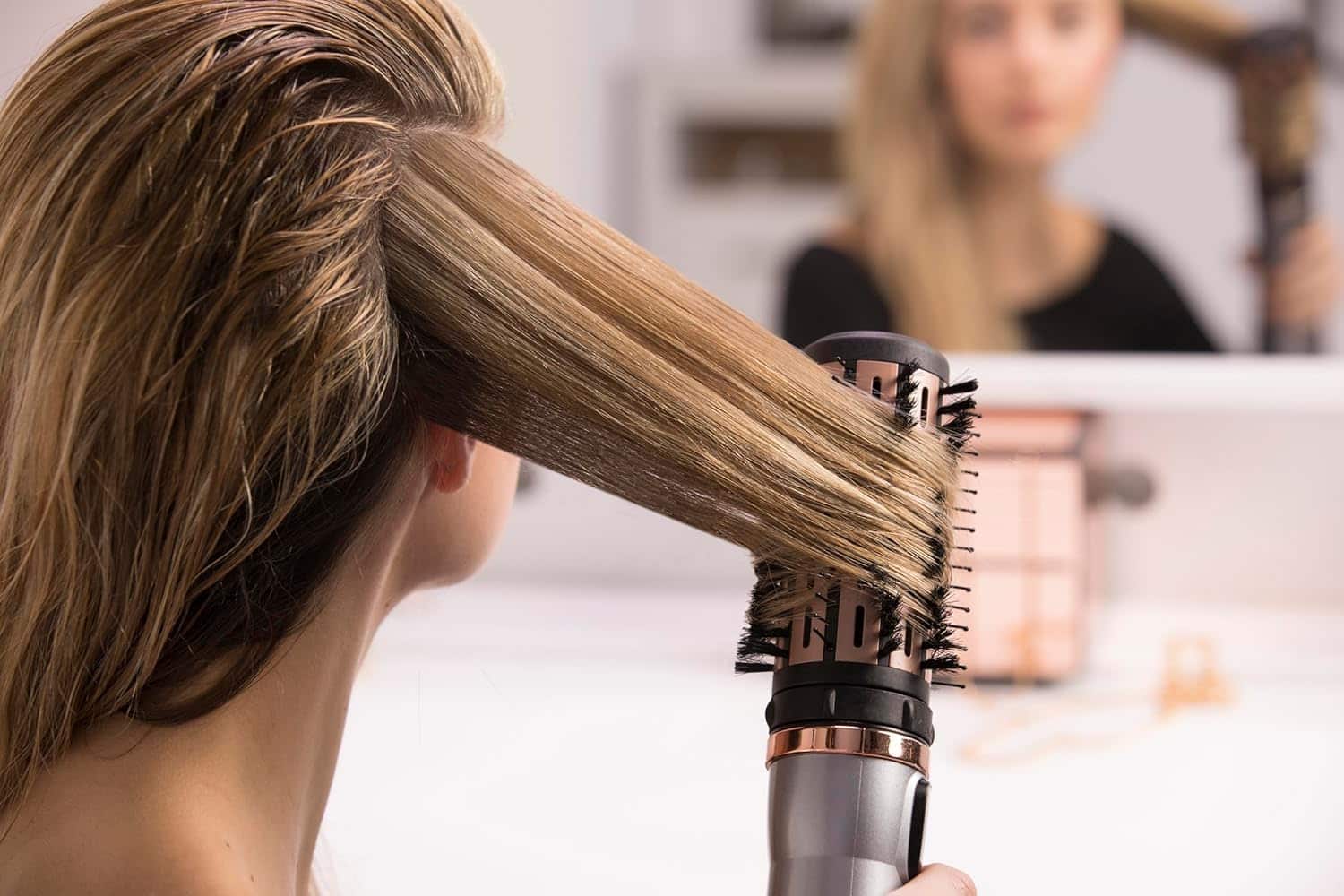 Une femme blonde en train de se coiffer à l'aide d'une brosse soufflante de la marque Remington.