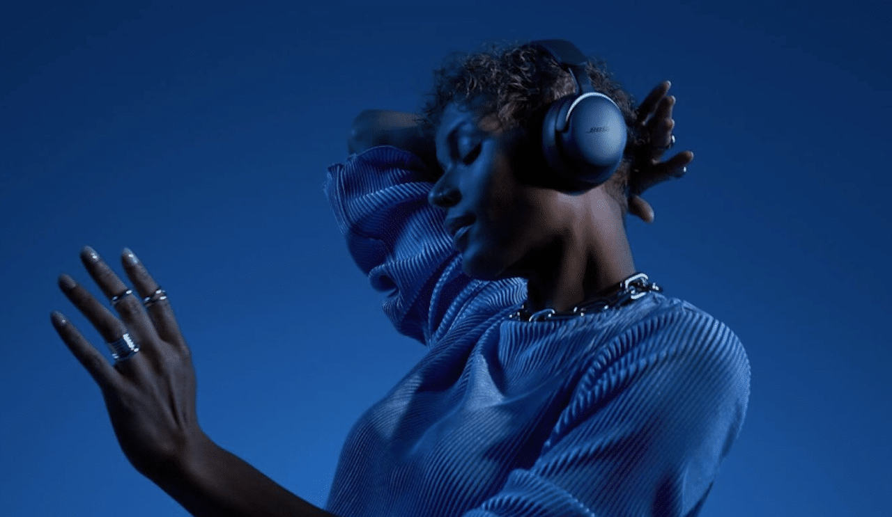 Une femme qui porte un casque audio de la marque Bose. Elle se tient devant un fond bleu.