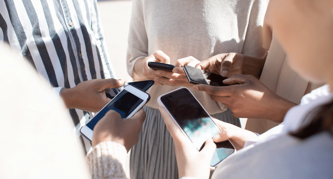 Un groupe de 5 personnes qui se tiennent en cercle et qui utilisent leur smartphone.