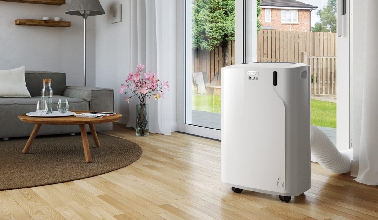 Un climatiseur mobile Delonghi dans un salon devant une baie vitrée et un sol en stratifié