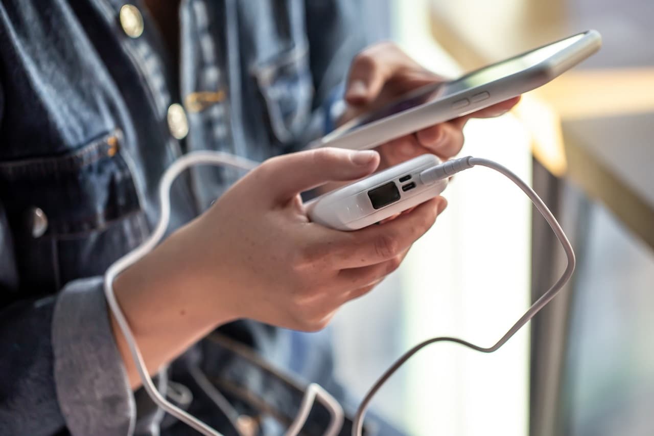 Une personne dont on ne voit pas le visage tient son smartphone dans une main et une batterie externe dans l'autre main