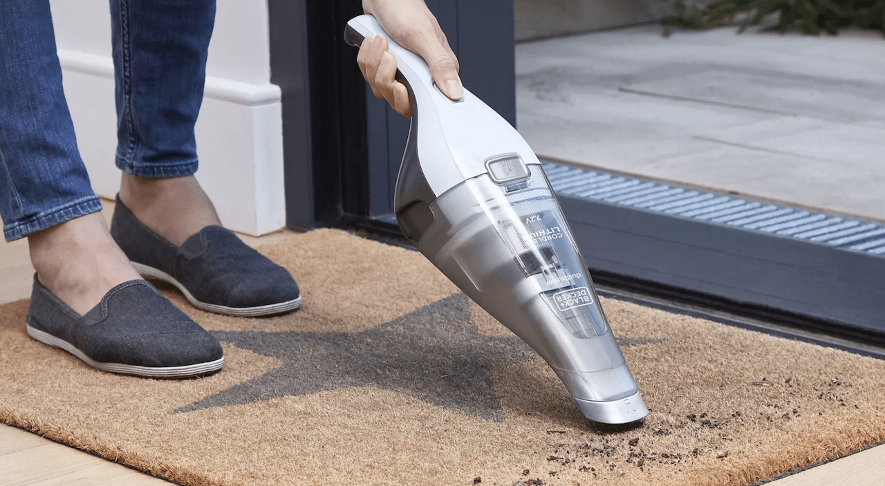 Une personne qui nettoie un petit tapis avec un aspirateur à main.